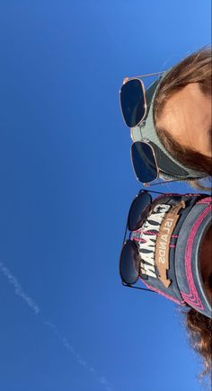 two people wearing sunglasses looking up into the sky with an airplane in the distance behind them