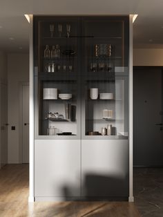 a glass cabinet with dishes and cups on it in the middle of a wood floored room