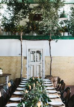 a long table set with place settings and greenery on the tables in front of an open door