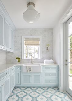 a blue and white kitchen with tile flooring, cabinets, sink and window in the corner