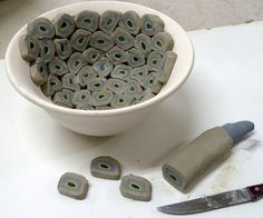 a white bowl filled with green beads next to a knife and some other items on a table