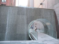 two people are walking up and down an escalator in a city with tall buildings