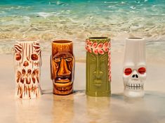 three different colored vases sitting on top of a sandy beach next to the ocean