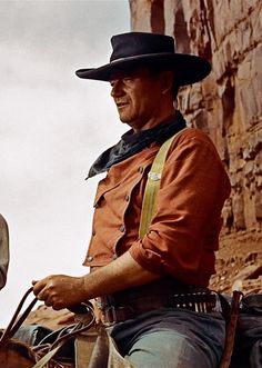 a man riding on the back of a brown horse next to a tall rock wall