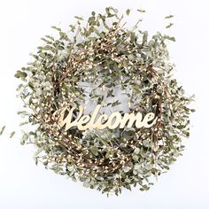 a wreath with the word welcome written in gold letters on it and some green leaves