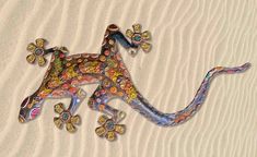 a colorful gecko sitting on top of sand covered in jewels and glass beads,