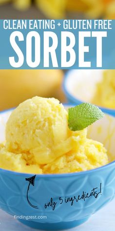 A small, vibrant blue bowl with yellow and white interior holding three scoops of a yellow sorbet that is garnished with mint. A fresh mango and additional bowl of sorbet is in the background.