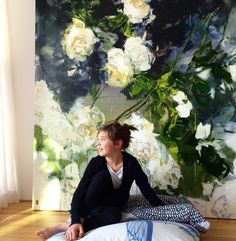 a woman sitting on top of a bed in front of a painting