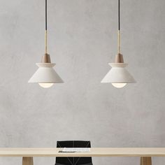 two pendant lights hanging over a table with a black chair in the foreground and a white wall behind it