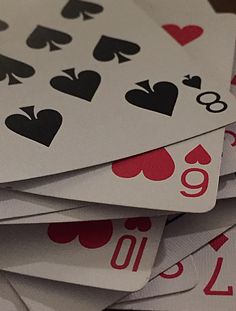 a pile of playing cards sitting on top of each other with numbers and hearts painted on them