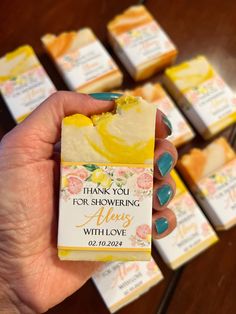 a hand holding a yellow and white soap bar with flowers on it, in front of rows of small ones