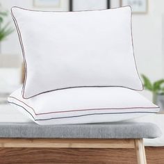 two pillows sitting on top of a bed next to a pillow case with red piping