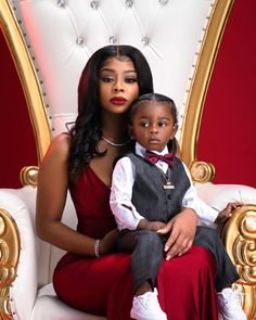 a woman in a red dress sitting on a white chair with a small child wearing a black bow tie