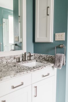 a bathroom with blue walls and marble counter tops, white cabinets and a large mirror above the sink