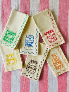 six hand embroidered tea towels on a pink and white striped tablecloth with different designs