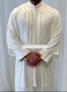 the man is wearing a white outfit and standing in front of a curtain with his hands on his hips