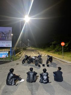 several people sitting on the side of a road with motorcycles parked in front of them