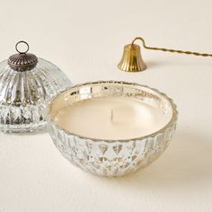 a glass bowl with a candle in it next to a small metal container on a white surface