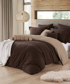 a bed with brown comforter and pillows in a room next to a window,