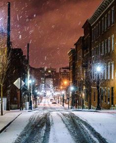 a snowy street at night with cars parked on the side and buildings in the background