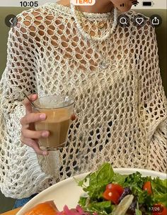 a woman holding a drink in her right hand while looking at the camera and eating salad