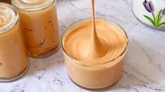 three jars filled with peanut butter on top of a marble counter next to two spoons