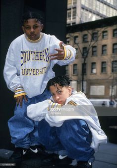 two young men sitting on top of each other in front of a building and one is pointing