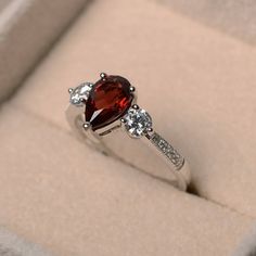 This ring features a 6*9mm pear cut natural garnet sterling silver finished with rhodium. Customization is available. It is made by hand, and it will take about 7 days to finish the ring after your payment is completed. Main stone: natural garnet weight: Approx 1.54 ct Metal type: sterling silver finished with rhodium Accent stone: cz Customization is available, I also can make it with 14k solid gold (white or yellow or rose) and diamond accent stone, just feel free to contact me. Any question, Garnet Wedding Rings, Garnet Wedding, Red Gemstone Ring, January Birthstone Rings, Garnet Engagement Ring, Emerald Cut Rings, Red Gemstones, January Birthstone, Twist Ring