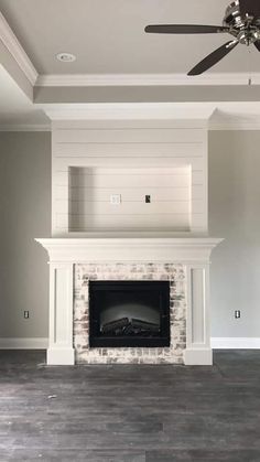 an empty living room with a fireplace and ceiling fan in the middle of the room