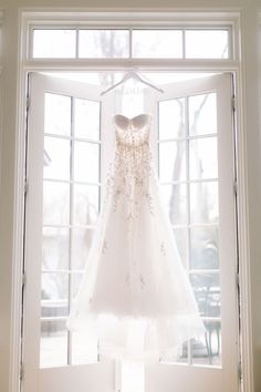 a wedding dress hanging on a window sill in front of a white door with the sun shining through it