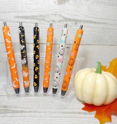 five pens are lined up next to an orange pumpkin