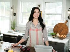 a woman standing in a kitchen next to a cutting board with fruit and vegetables on it