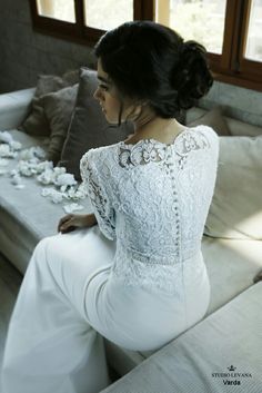 a woman sitting on top of a couch wearing white pants and a long sleeved dress