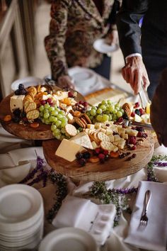 two people are cutting into a platter full of cheese and crackers on a table