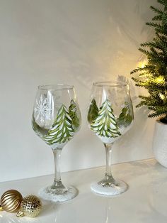 two wine glasses decorated with christmas trees and snowflakes are sitting next to a potted plant