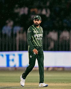 a man in green and white uniform walking across a field