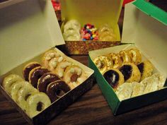 three boxes filled with different types of doughnuts on a wooden table next to each other