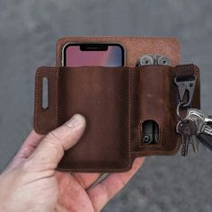 a hand holding a brown leather wallet with keys and cell phone in the other side