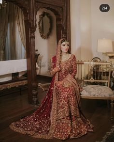 a woman in a red and gold bridal gown sitting on a bed next to a mirror