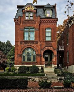 an old brick building with many windows and steps leading up to the front door is surrounded by greenery