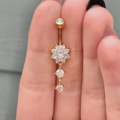 a woman's hand holding a gold navel ring with three diamonds on it