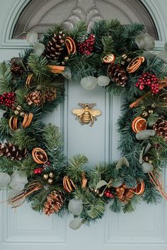 a christmas wreath with pine cones, berries and a bee hanging on the front door