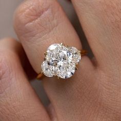 a woman's hand with a diamond ring on top of her finger and an oval shaped diamond in the middle