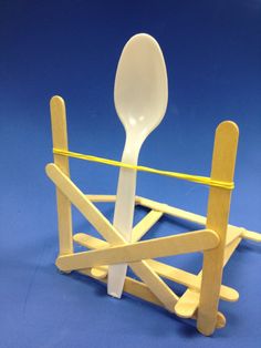 a white spoon and fork in a wooden holder with yellow tape on the side,