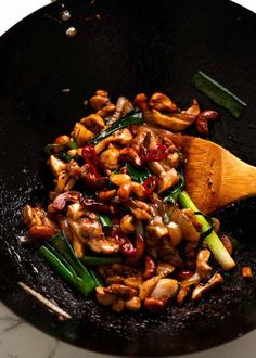 chicken and vegetables cooking in a wok with a wooden spoon