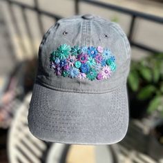 a gray hat with blue and purple flowers on it sitting on top of a table