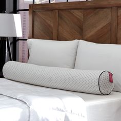 a white bed with pillows on it and a pillow in front of the headboard