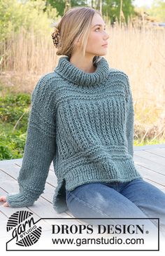 a woman is sitting on the ground wearing a green knitted sweater and blue jeans