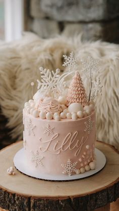 A pastel pink Winter ONEderland cake decorated with white snowflakes, edible pearls, a frosted pink tree, and the name “Lilly” written in cursive, sitting on a rustic wood slice. Perfect for a first birthday celebration. Onederland Cake, Onederland Party, Edible Pearls, Frosted Tree, Winter Onederland, Pink Cake, Tree Topper, Cake Ideas, Birthday Celebration