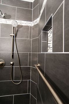 a shower head and hand rail in a gray tiled bathroom with stainless steel fixtures on the wall